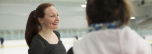 Allison smiling while talking to her coach on the ice. Image for the manleywoman skatecast, a figure skating podcast